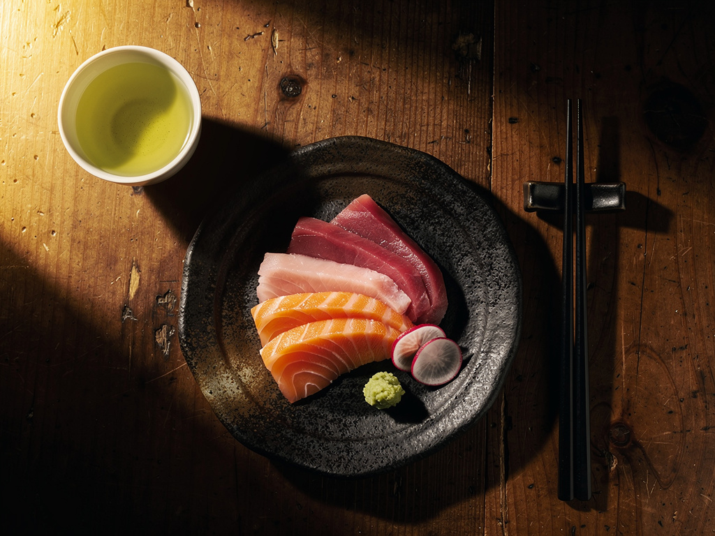 A diner's table with an elegant plate of sashimi, chopsticks and a cup of green tea